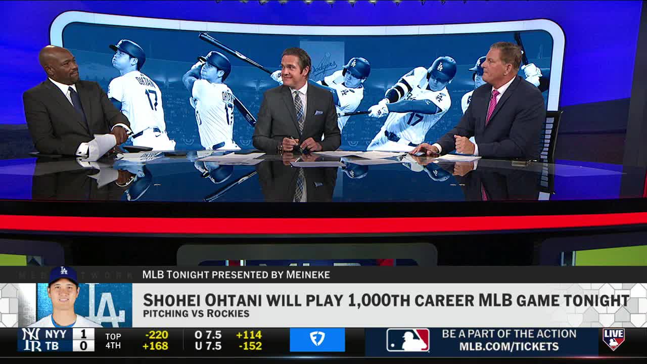 Three men in suits sit at a desk on the MLB Network set, discussing Shohei Ohtani. Behind them, a blue screen displays a series of images of a player swinging a bat.
