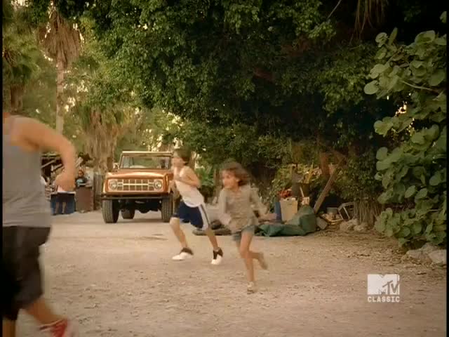 Kids sprint down a dirt road, their feet kicking up dust. A vintage orange Bronco sits parked nearby, and the MTV Classic logo is visible in the corner.
