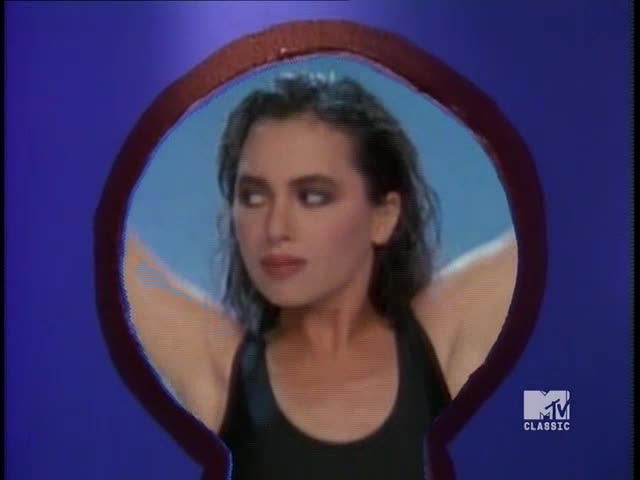 Framed by a keyhole, a woman in a black top raises her arms, her gaze slightly off-center. The MTV Classic logo is visible in the corner, a familiar sight from the U.S.
