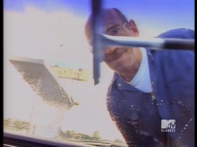 A man in a blue uniform is squeegeeing a windshield. The sky is bright, and the MTV Classic logo is visible in the corner.
