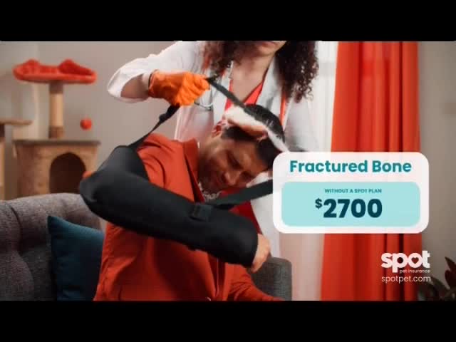 A person in a red shirt sits on a couch, wearing a black sling with a bandage on their head. A medical professional in a lab coat and orange gloves is adjusting the sling.
