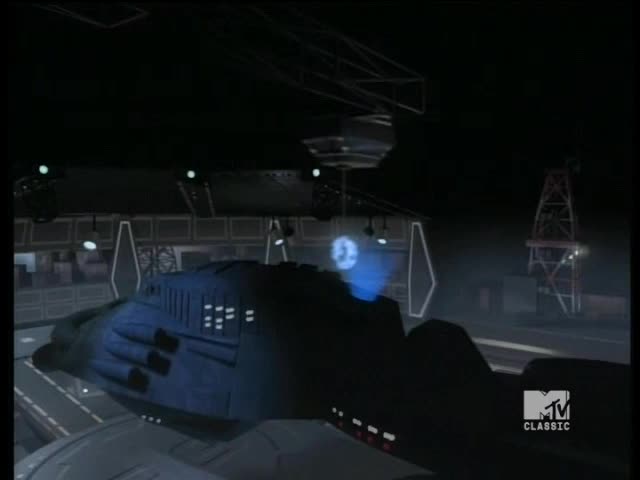 A dark blue, futuristic craft sits on a platform, a glowing blue light emanating from its side. The MTV Classic logo is in the corner, so it's probably a scene from a show.
