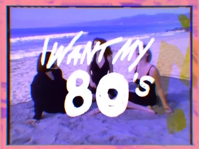 Three women in black swimsuits sit on a beach, with the ocean in the background. Bold, white text reading "I WANT MY 80's" is scrawled across the image.
