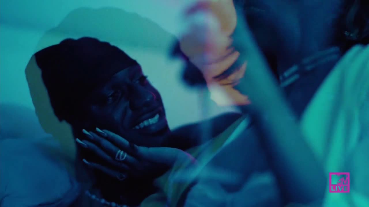 A man in a black cap is smiling as someone's hand touches his cheek. The MTV Live logo is visible in the corner.
