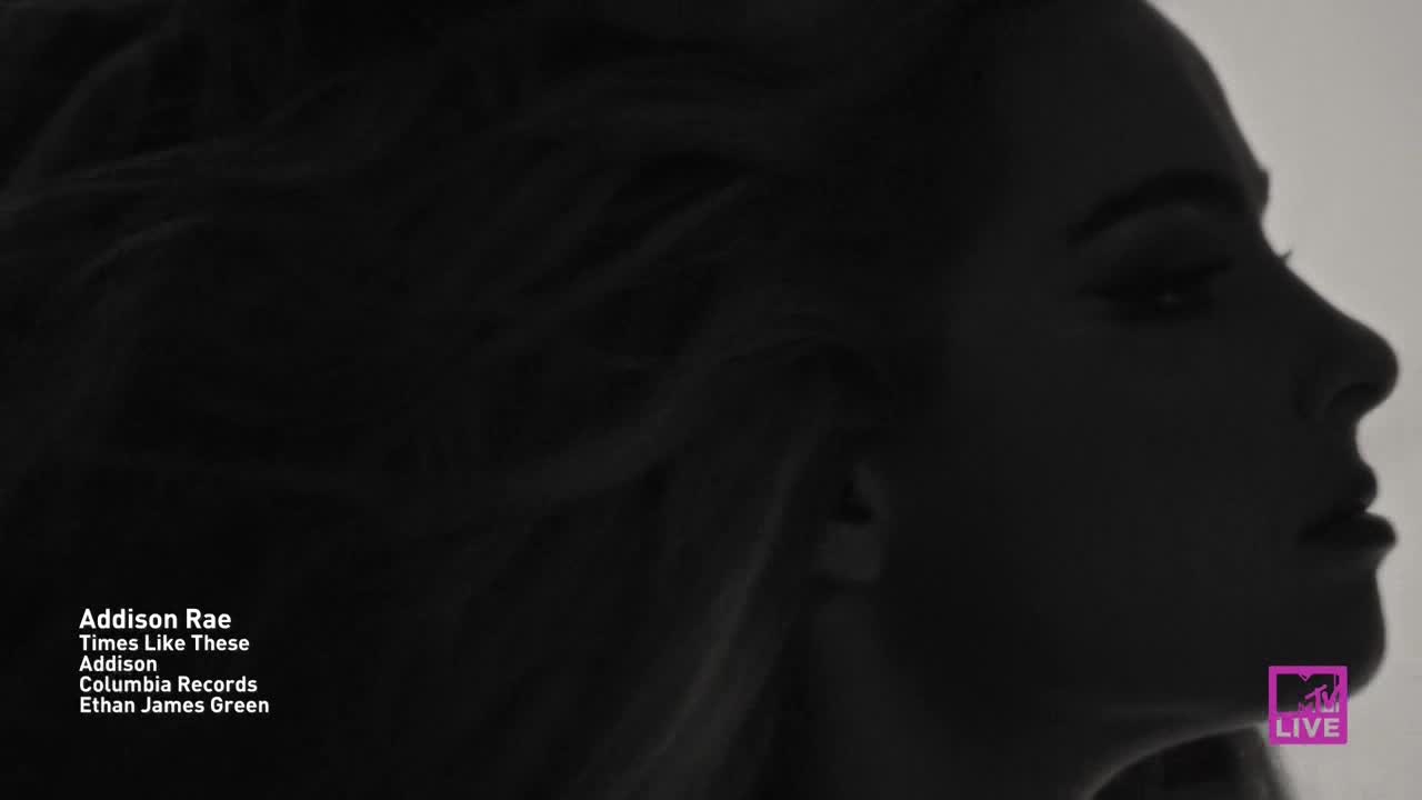 Addison Rae's profile is silhouetted against a bright background on MTV Live. Her hair flows around her face, and the camera focuses on her features in the dark.

