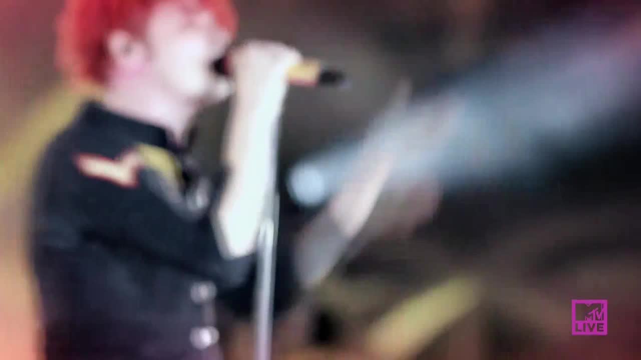 A man with bright red hair sings into a microphone, illuminated by a spotlight. The MTV Live logo sits in the corner as the band performs.
