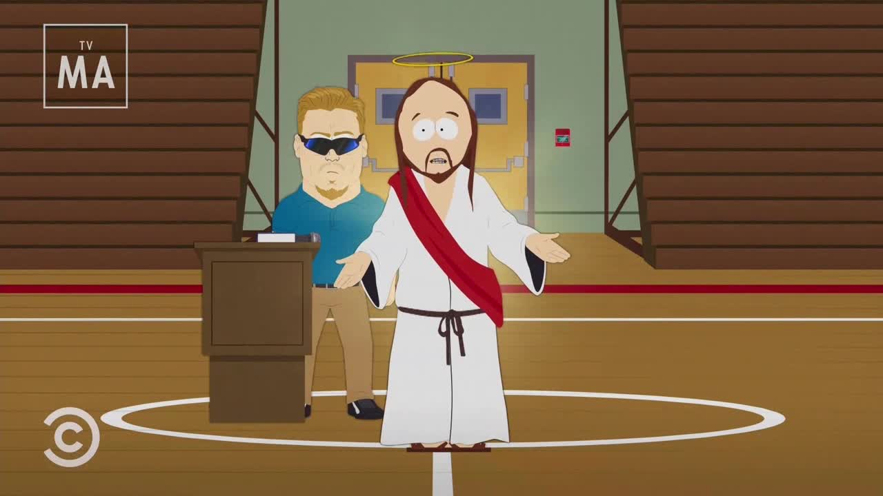 Jesus, in his usual attire, stands with his arms outstretched, looking bewildered on a basketball court. A man in sunglasses stands behind a podium, seemingly providing support or protection.
