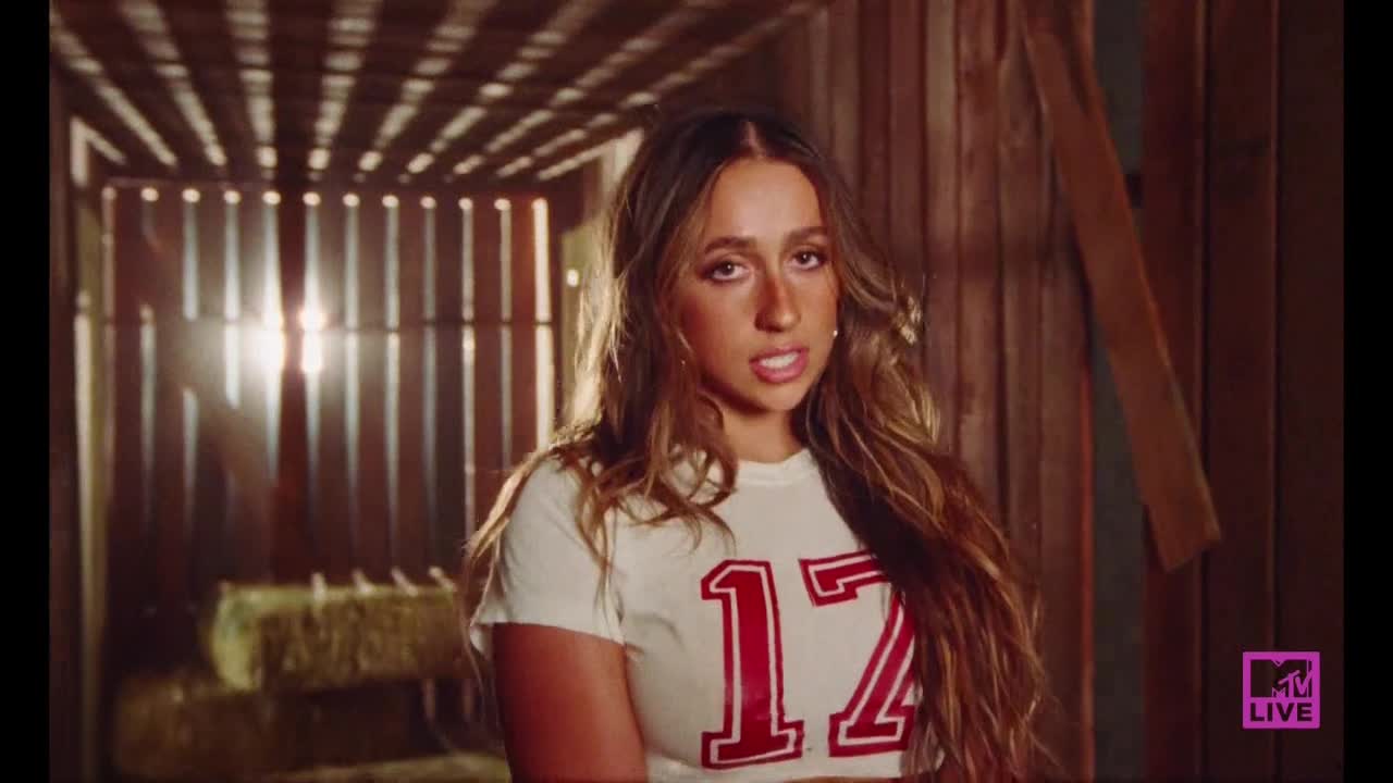She's standing in a barn, the sunlight streaming through the slats behind her. Her jersey has a big red "17" on it, and she's talking directly to the camera.
