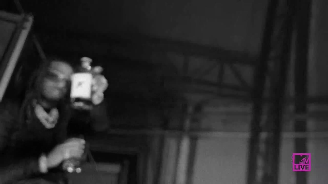 A person, slightly out of focus, holds up a bottle with a white label. The MTV Live logo sits in the lower right corner of the frame.
