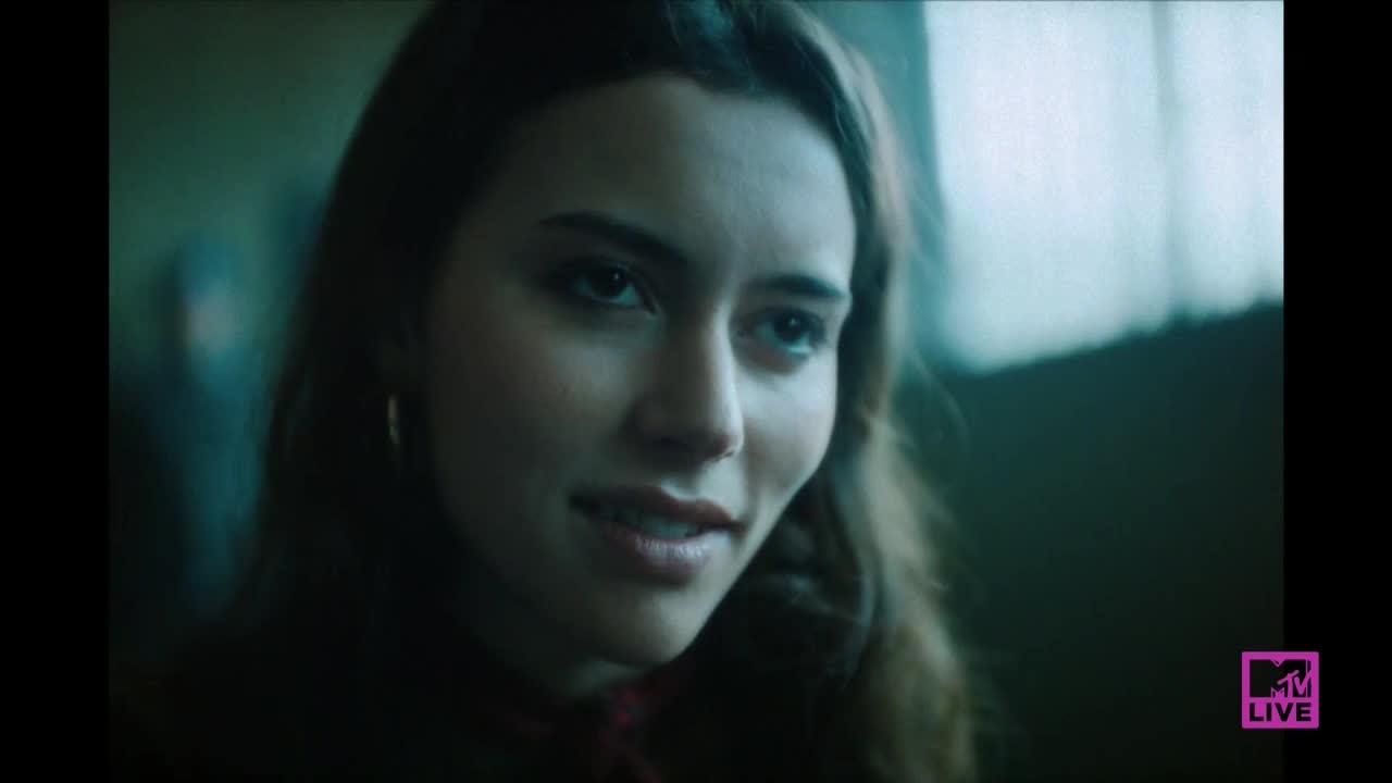 A young woman with long, dark hair is looking towards me, her lips slightly parted in a subtle smile. The MTV Live logo is in the bottom right corner.
