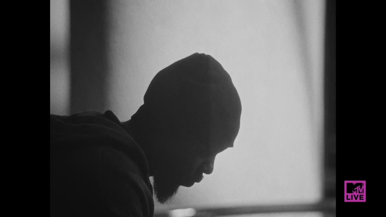 A man in a beanie is silhouetted against a bright background. He's looking down, his face partially obscured by the shadows.
