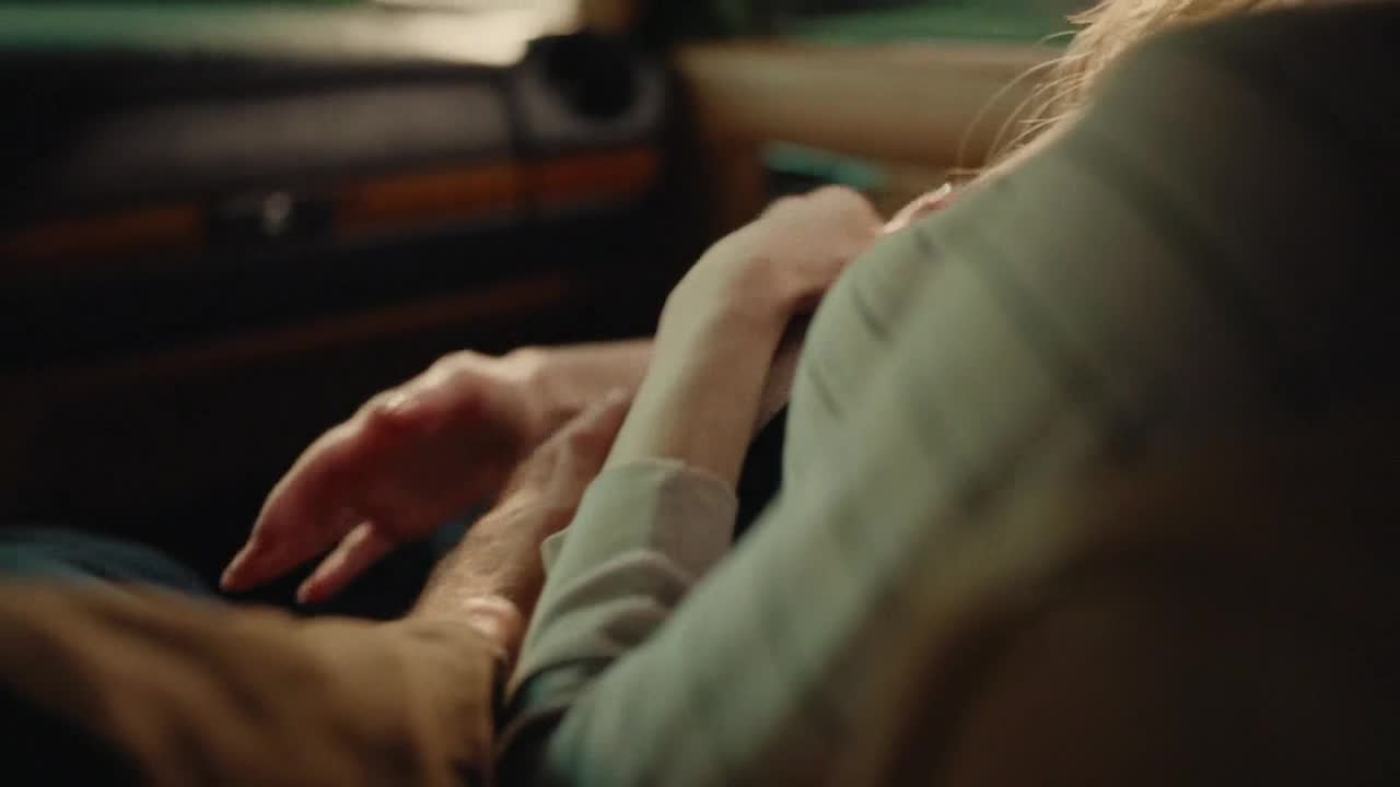 A hand rests on another, fingers intertwined. The light catches the skin, highlighting the gentle touch.
