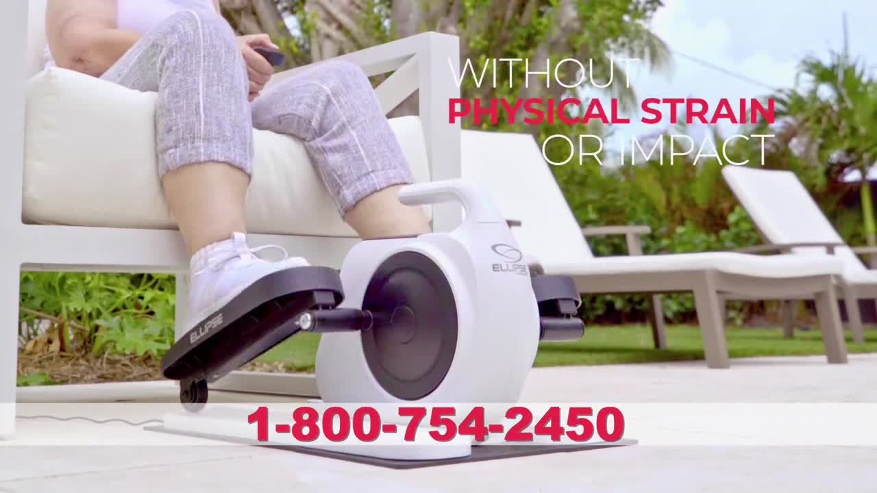 Someone is sitting on a white outdoor chair, pedaling a small, white exercise machine. The machine's pedals are moving back and forth, and the person's feet are in white sneakers.

