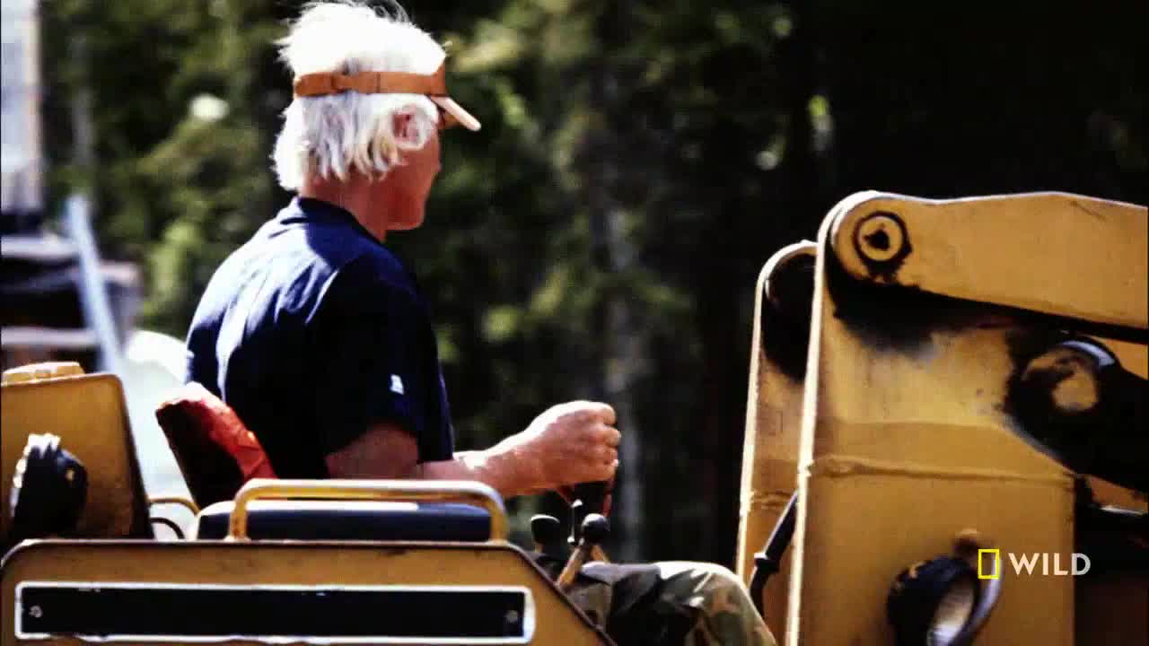 A man in a visor grips the controls of a yellow machine. He's looking to the side, focused on the task ahead, as if on a National Geographic Wild special.

