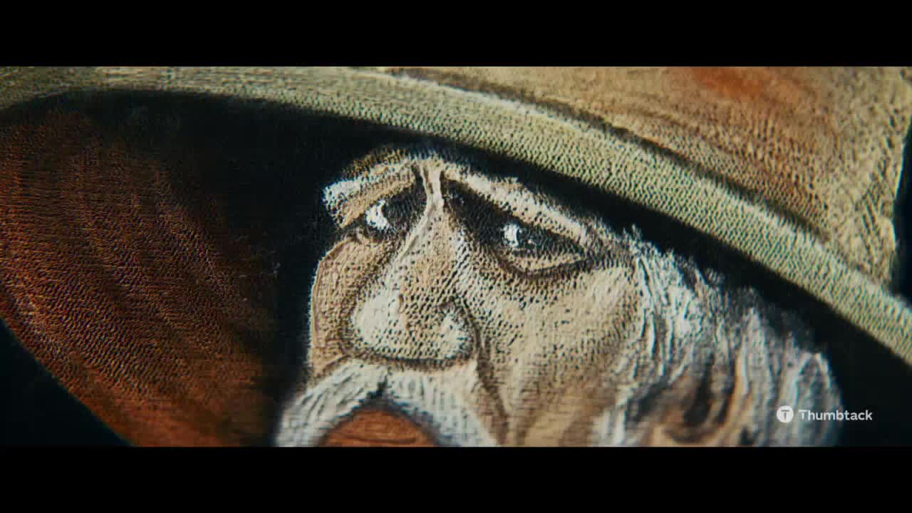 A detailed drawing of an older man's face fills the frame, his eyes filled with a melancholic expression. He's wearing a wide-brimmed hat, and the texture of the artwork is visible in the close-up.
