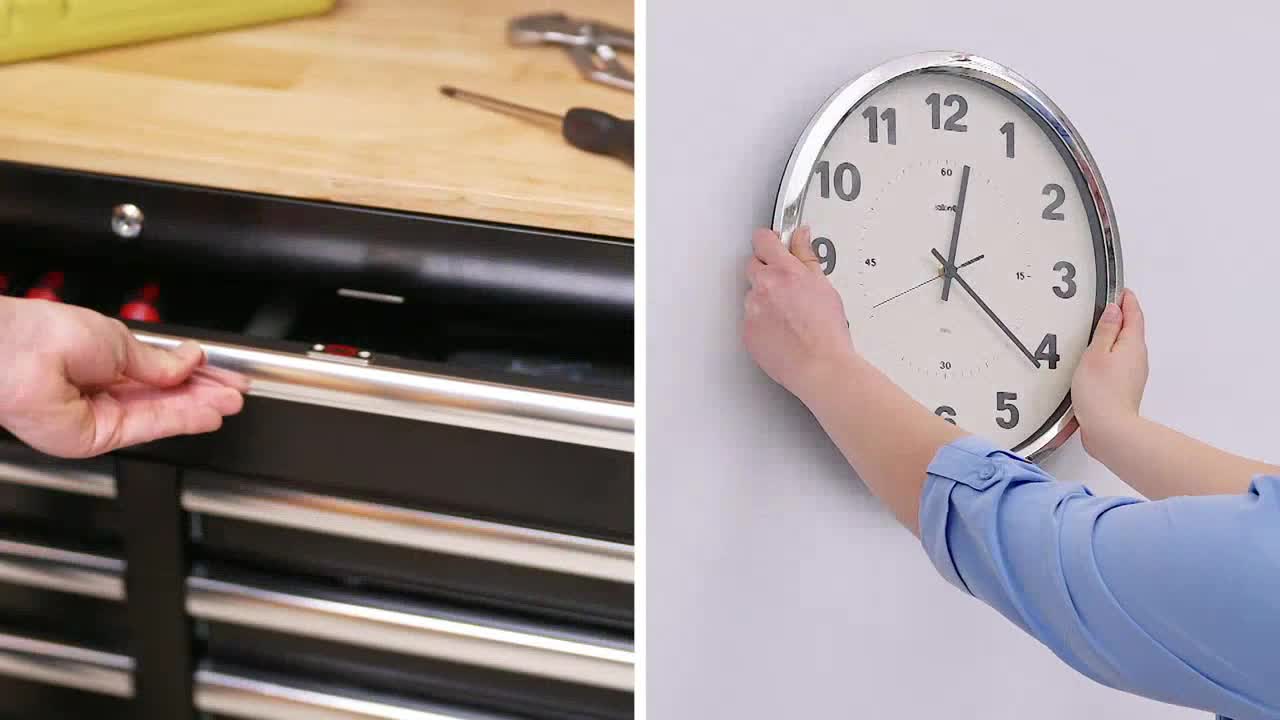 Someone is pulling open a drawer on a black toolbox, while another person holds a clock against a white wall. The clock's hands point to just after 12:25.

