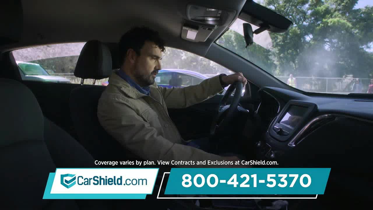 A man sits in the driver's seat, gripping the steering wheel with both hands. He's looking down, perhaps concentrating on something just out of view.

