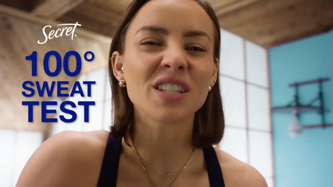 A woman is looking directly at the camera, smiling, and speaking. Large blue text declares a "100° SWEAT TEST" next to her.
