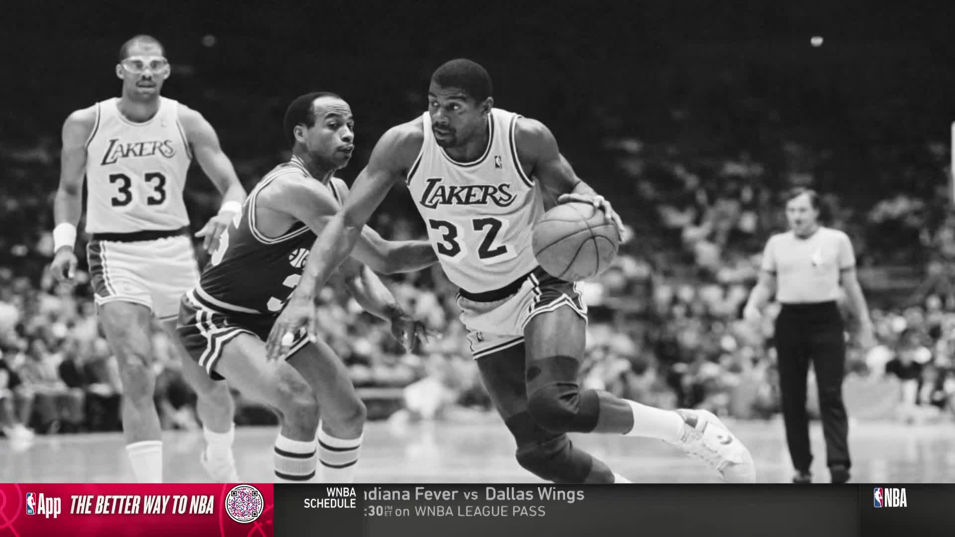 Magic Johnson, in a Lakers jersey, dribbles the ball, driving toward the basket. A defender in a dark jersey tries to stay with him, while Kareem Abdul-Jabbar, wearing glasses, trails behind.
