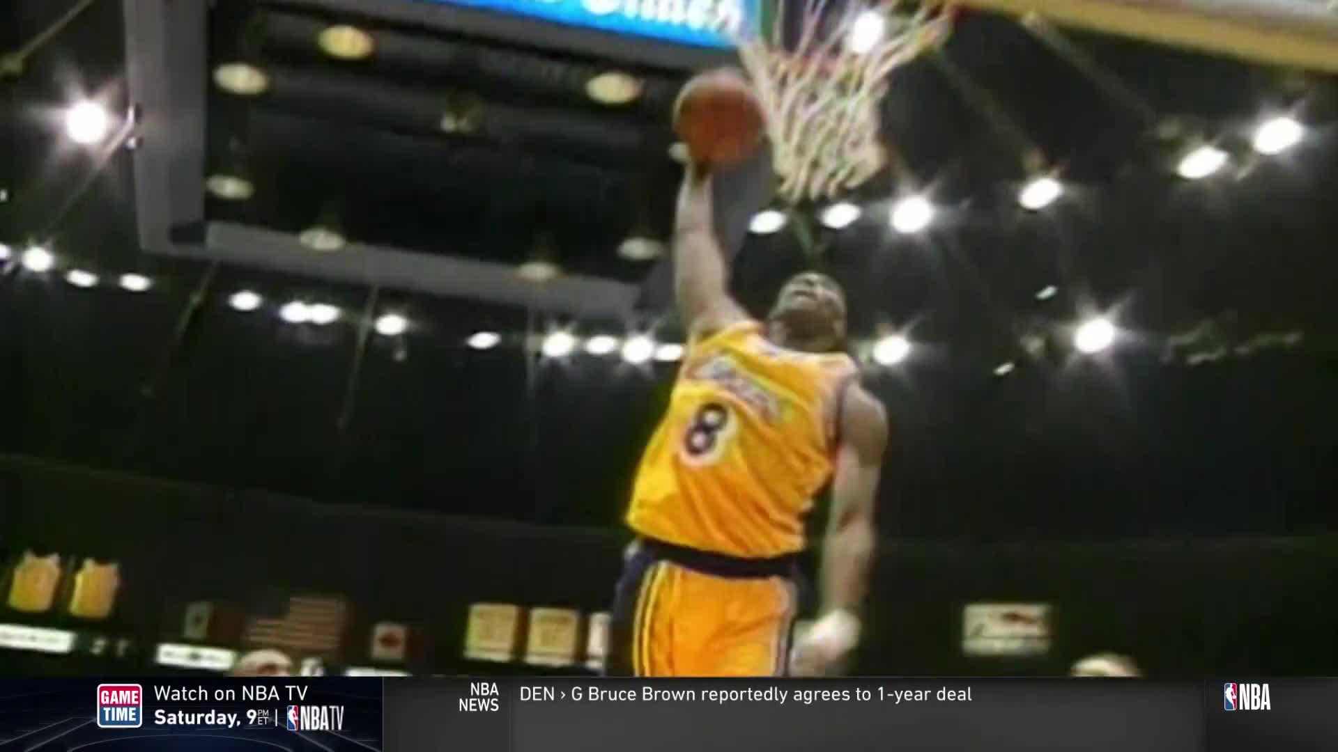 A player in a yellow jersey with the number 8 is soaring toward the basket. The ball is extended above his head, about to go through the net.
