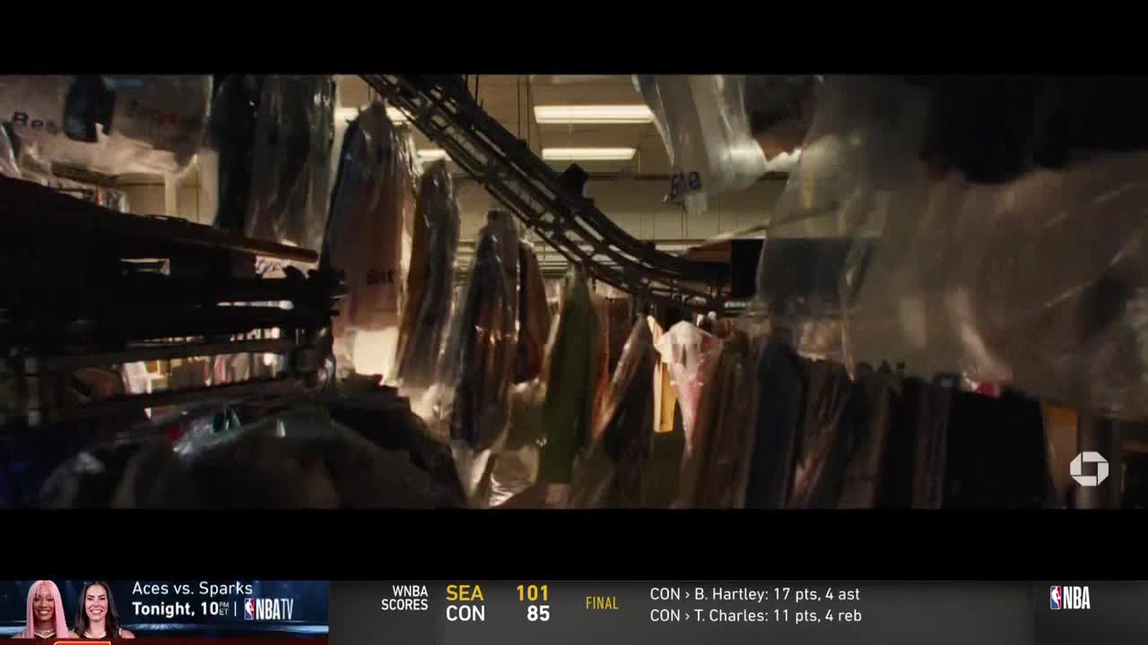 Rows of garments, encased in plastic, hang from an overhead rack. The scene is dimly lit, with the NBA TV logo in the corner.
