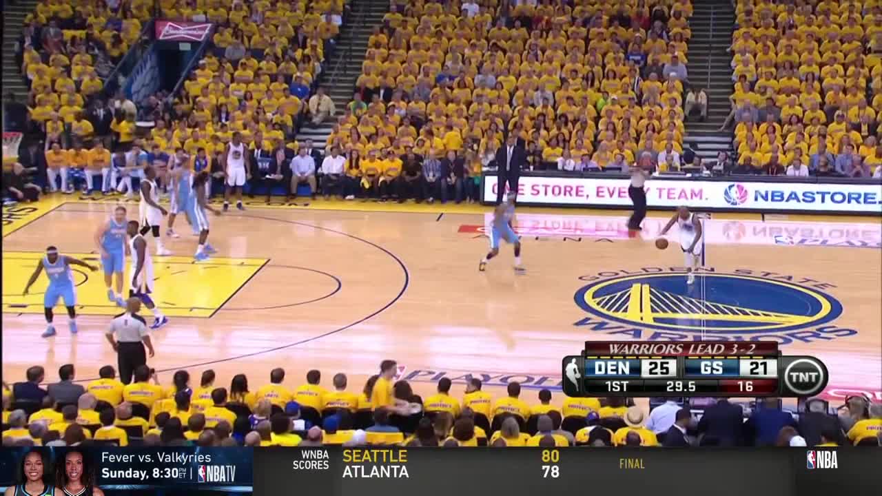A player in a light blue jersey dribbles the ball towards the basket, while a referee watches closely. The crowd in the stands is a sea of yellow shirts, and the scoreboard shows the Warriors leading.
