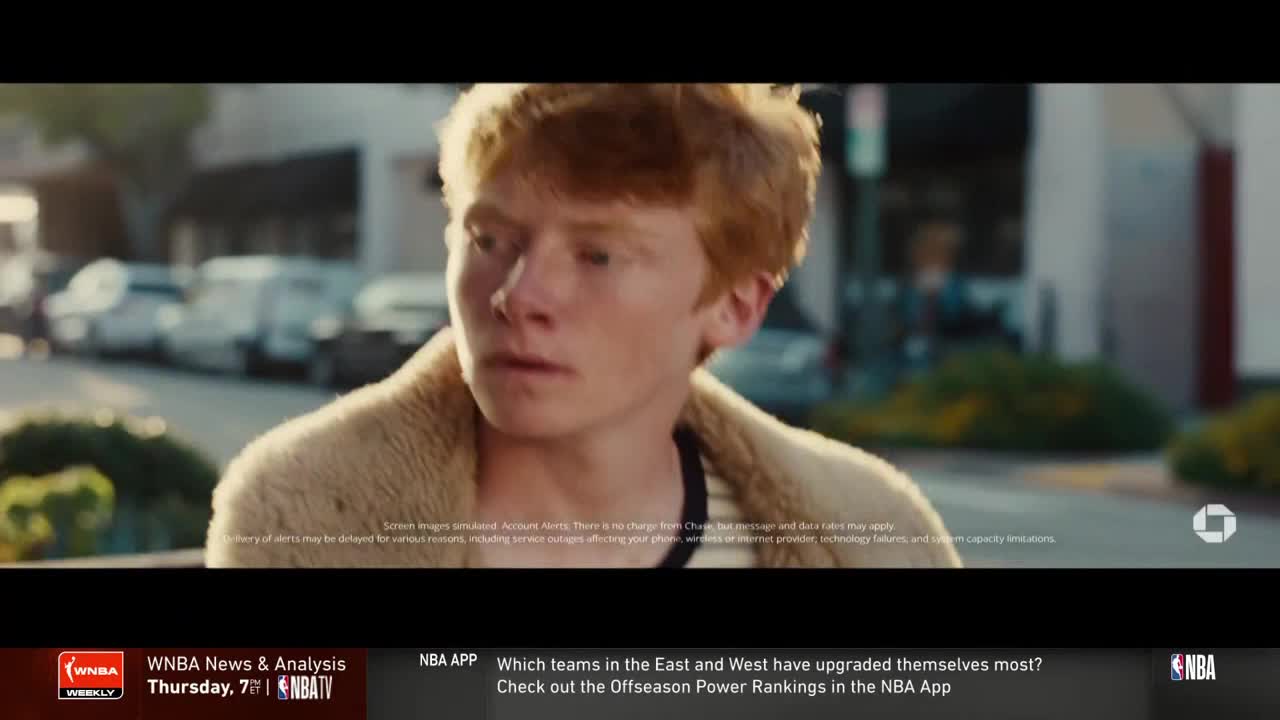 A young man with red hair looks slightly off-camera, wearing a tan coat. The scene appears to be a commercial break on NBA TV, with the WNBA news and NBA app information displayed at the bottom.
