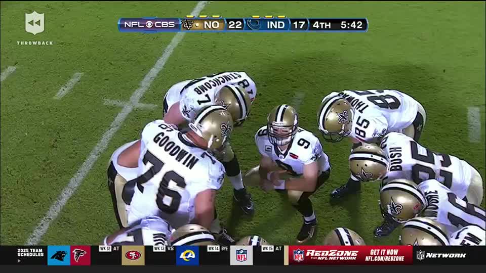 The New Orleans Saints huddle around their quarterback, the gold helmets reflecting the stadium lights. The scoreboard on the NFL Network shows the Saints leading the Colts in the fourth quarter.

