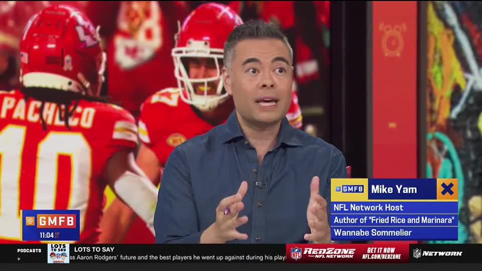 A man in a blue shirt gestures animatedly, speaking on the NFL Network's "Good Morning Football." Behind him, players in red uniforms are visible, their backs to the camera.
