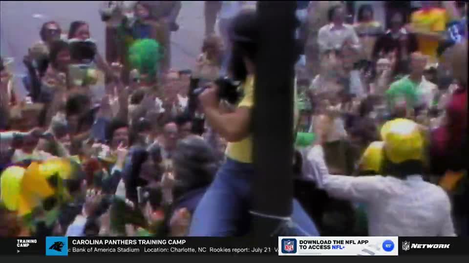 A crowd of people, many with their hands raised, surrounds a person holding a camera. The scene is part of the Carolina Panthers Training Camp, as shown on NFL Network.
