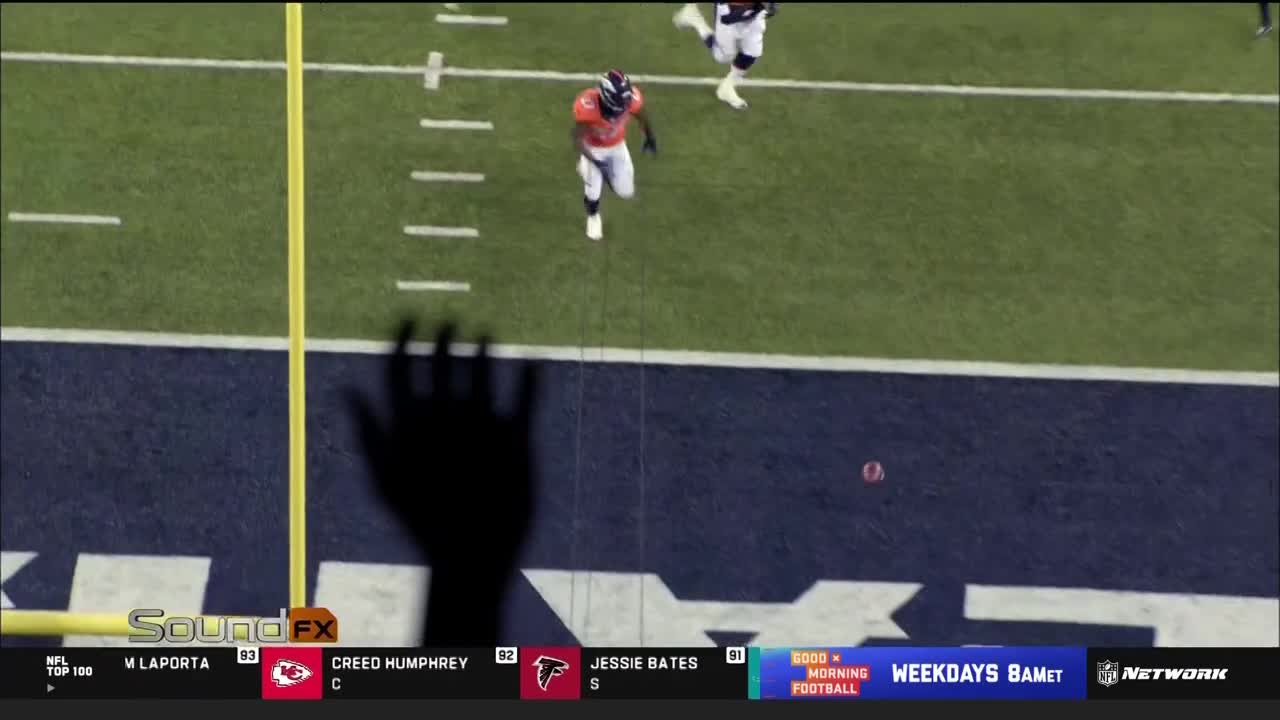 A player in an orange and blue uniform sprints toward the end zone. The football sits on the ground, and a shadow of a hand looms over the field.

