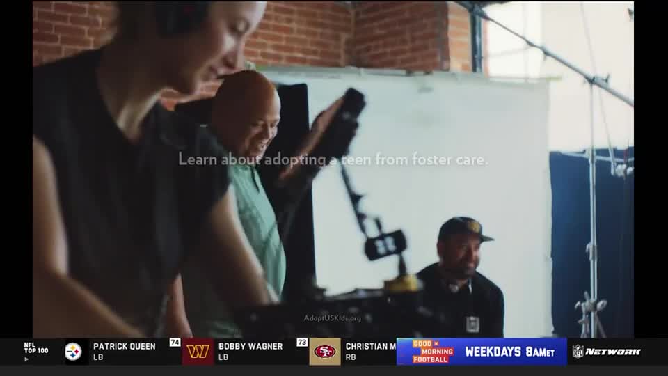 A person in a black shirt adjusts a camera, while another man in a green shirt looks on. The NFL Network logo is visible at the bottom, along with text about adopting teens.
