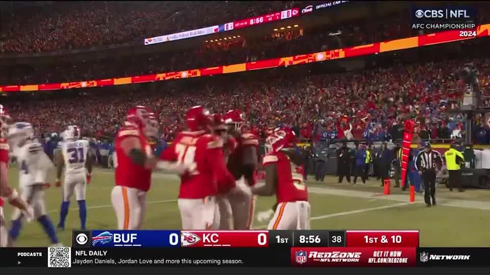 The Chiefs, in red, are huddled together on the field, celebrating. Across the field, the Bills' defense is standing around, watching.
