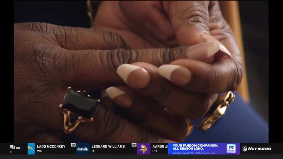 The hands, adorned with a large black ring, are clasped together. The French-tipped nails are prominent as the hands rest, likely during an NFL Network broadcast.
