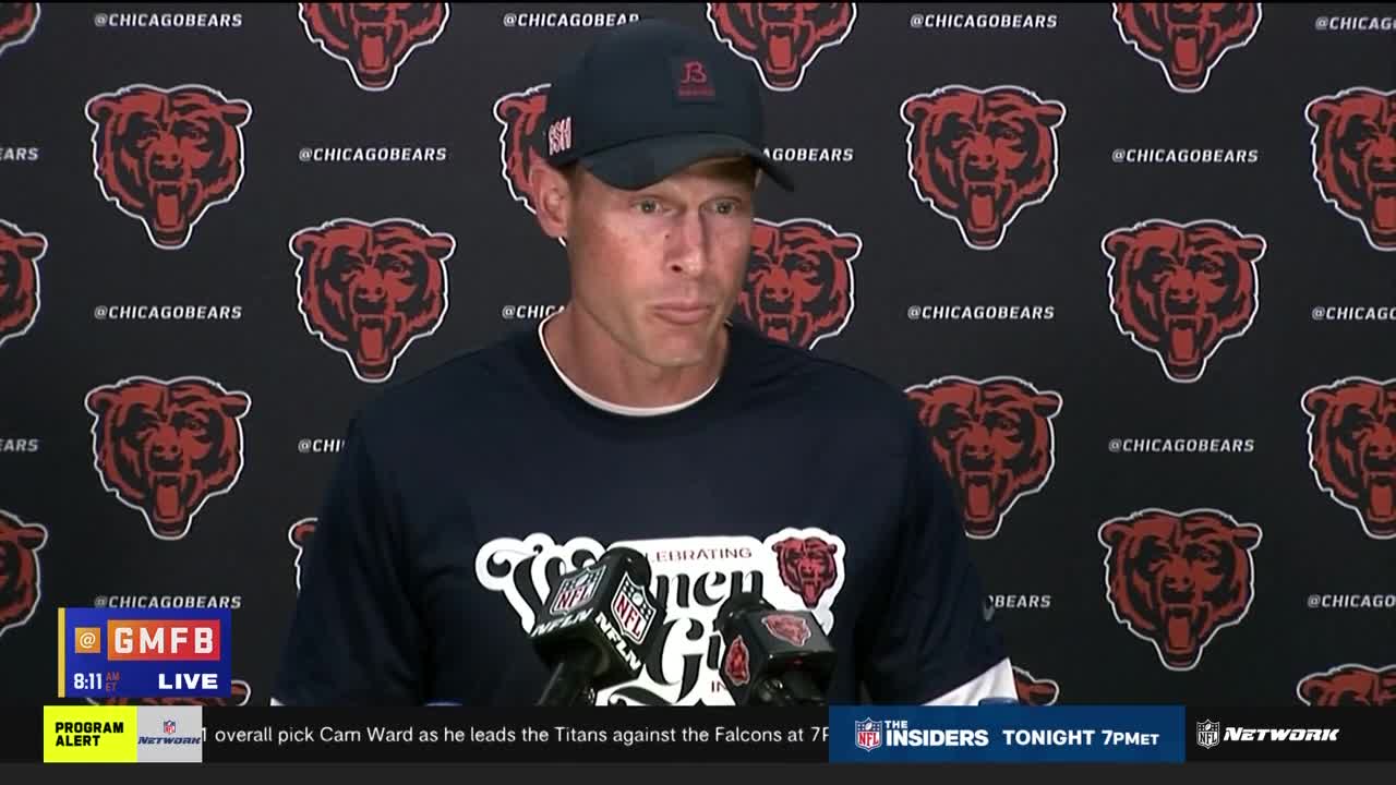 A man in a Bears cap and shirt stands at a podium, speaking into microphones with an NFL Network logo. Behind him, a backdrop is covered in Chicago Bears logos.
