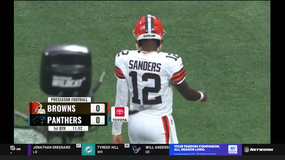 A Cleveland Browns player, wearing number 12, walks toward the sideline. The scoreboard on NFL Network shows the Browns and Panthers are tied at zero in the first quarter.
