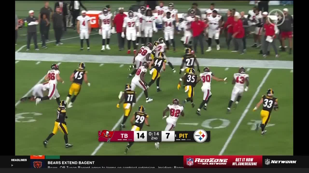 A player in black and yellow is being tackled near the sideline, while others in white and red pursue the play. The scoreboard on the NFL Network shows the score and time remaining in the second quarter.
