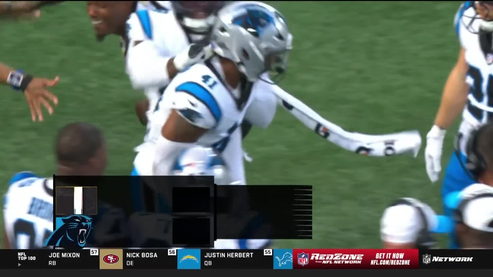 A Carolina Panthers player in a silver helmet and white jersey is celebrating with teammates. He's extending his arm, the white sleeve of his uniform stretched out.

