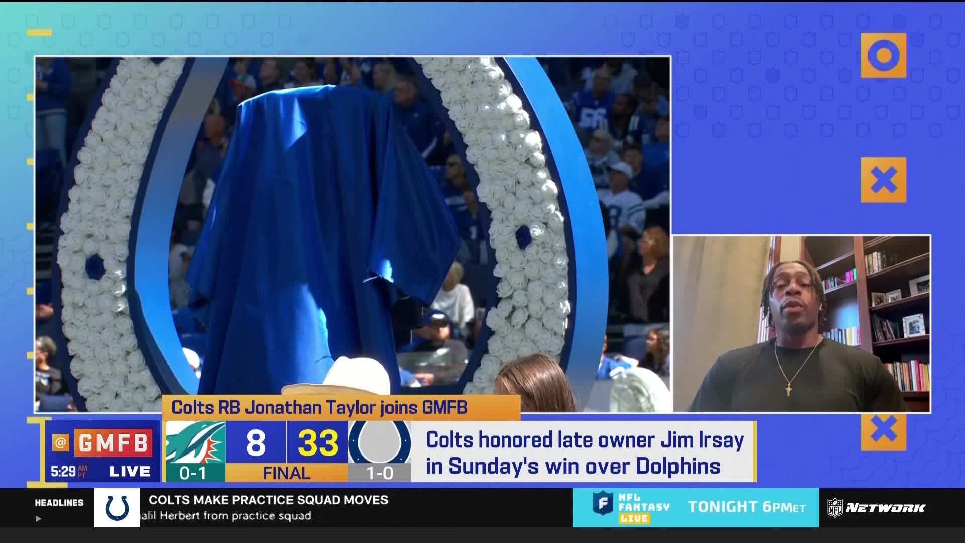 A blue cloth covers something in front of a large, white-flowered arch. On the right, a man is speaking on NFL Network's "Good Morning Football" set.
