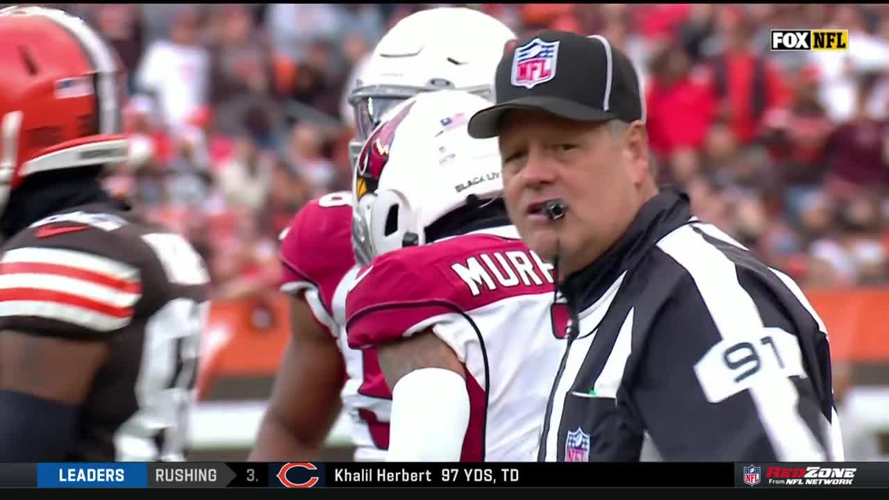 An NFL referee, whistle in mouth, looks toward the field as players in red and brown uniforms stand nearby. The RedZone graphic at the bottom of the screen shows a Chicago Bears touchdown.
