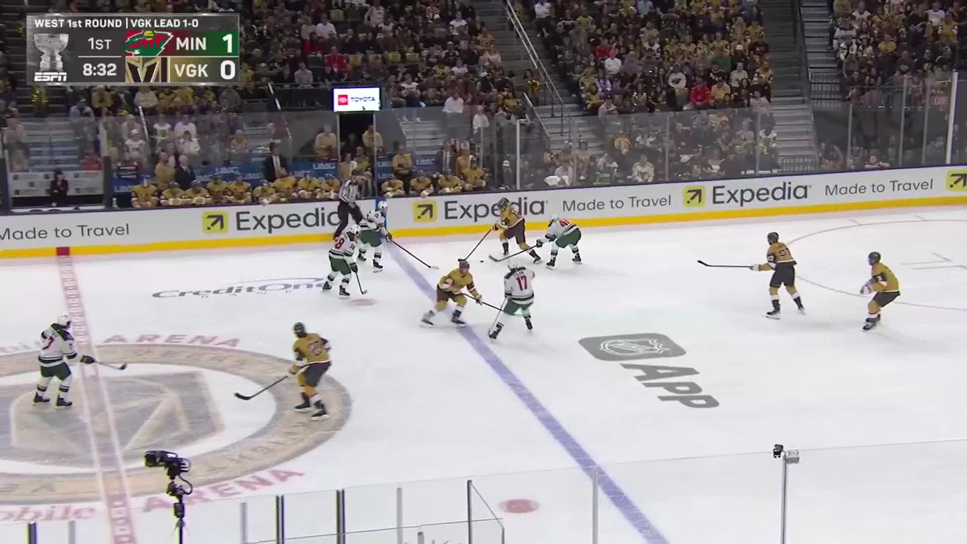 The Minnesota Wild, in green and white, are on the attack, trying to get the puck past the Vegas Golden Knights' defense. The puck is in the neutral zone, and both teams are battling for possession.
