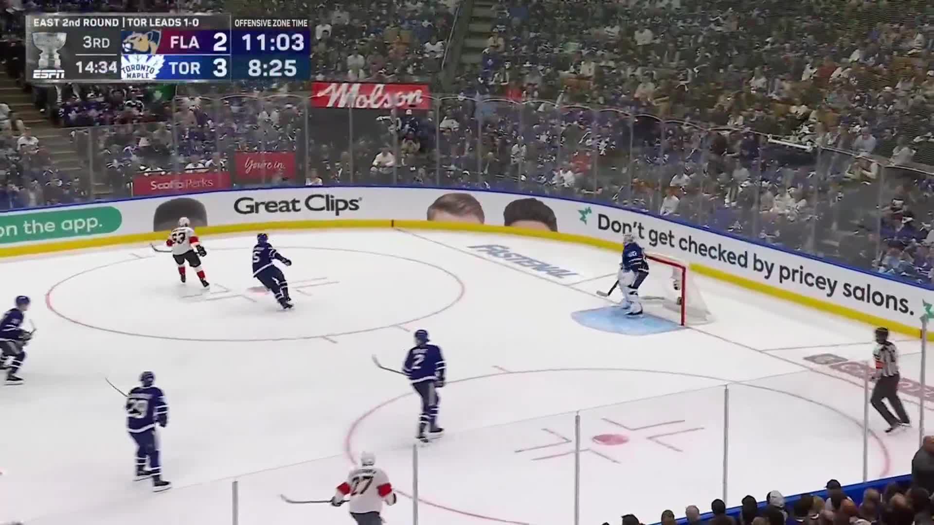 The Toronto Maple Leafs are on offense, with a player in blue skating toward the net. The goalie is ready, and the referee is watching the play unfold.
