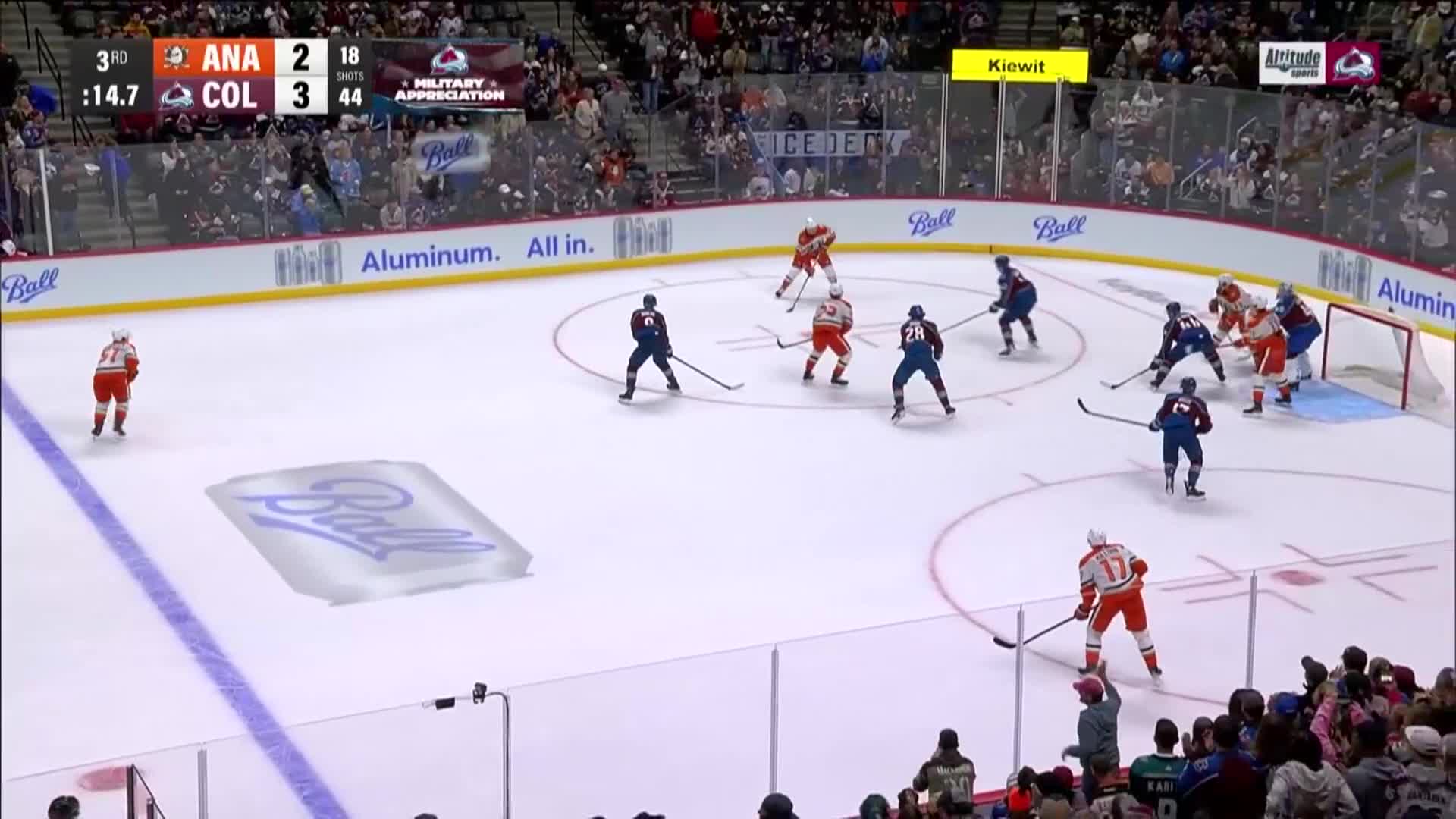 The Ducks in orange are pressing toward the net, while the Avalanche in blue defend. The puck is near the goal, and both teams are battling for possession.
