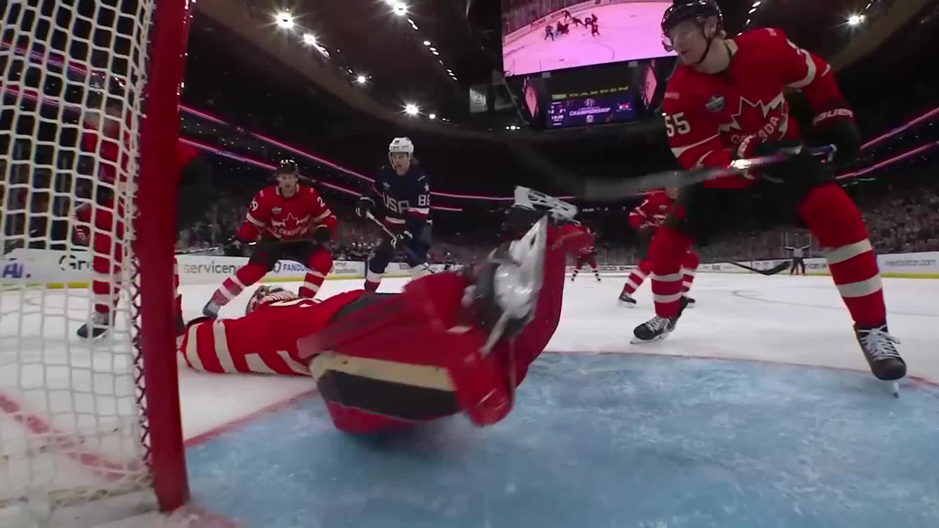 The goalie, sprawled out in red, is horizontal in the crease. A player in red, stick raised, appears ready to shoot at the net.
