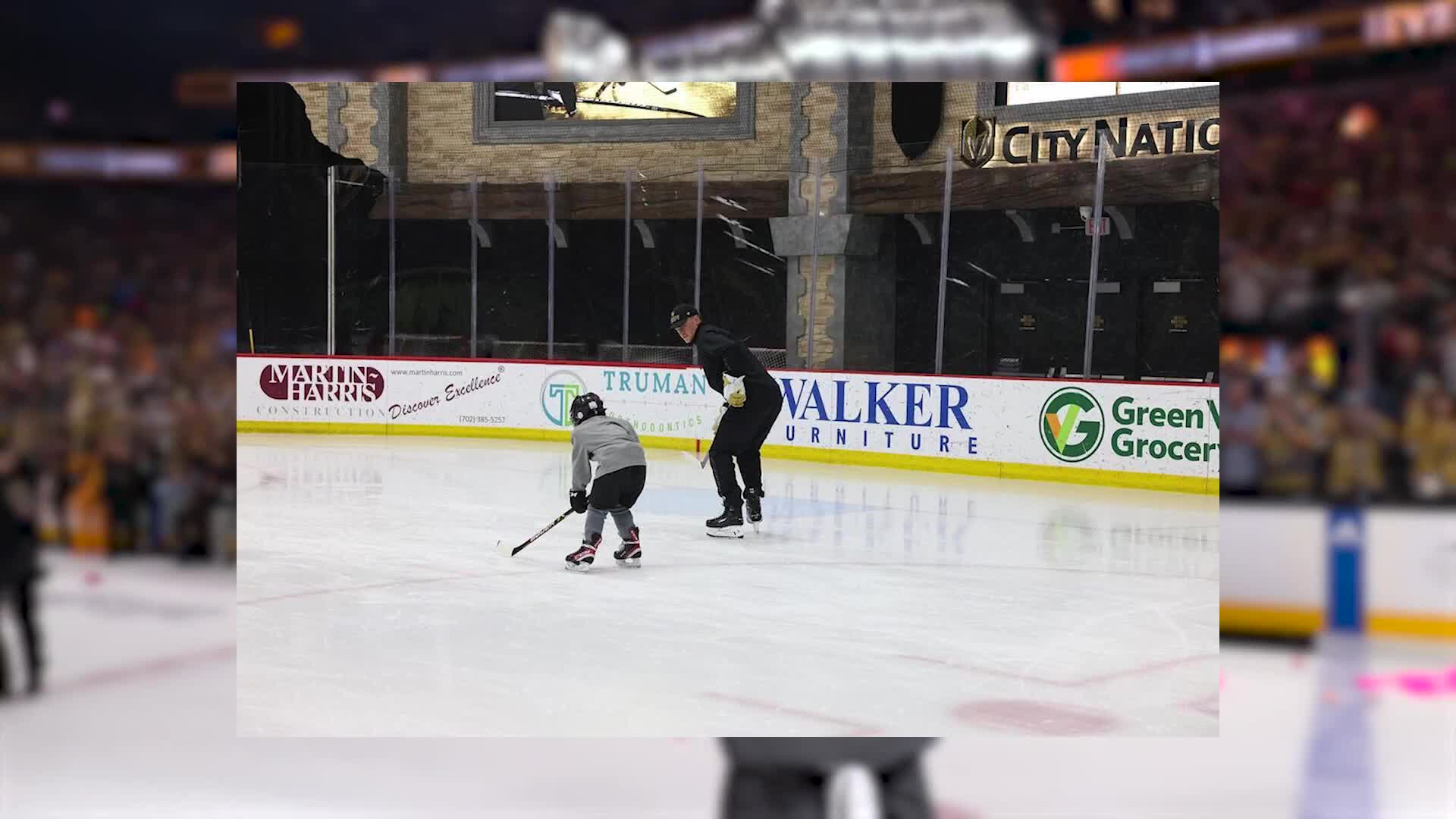 A young hockey player, stick in hand, glides across the ice, while a coach watches nearby. The arena's boards display advertisements for local businesses.
