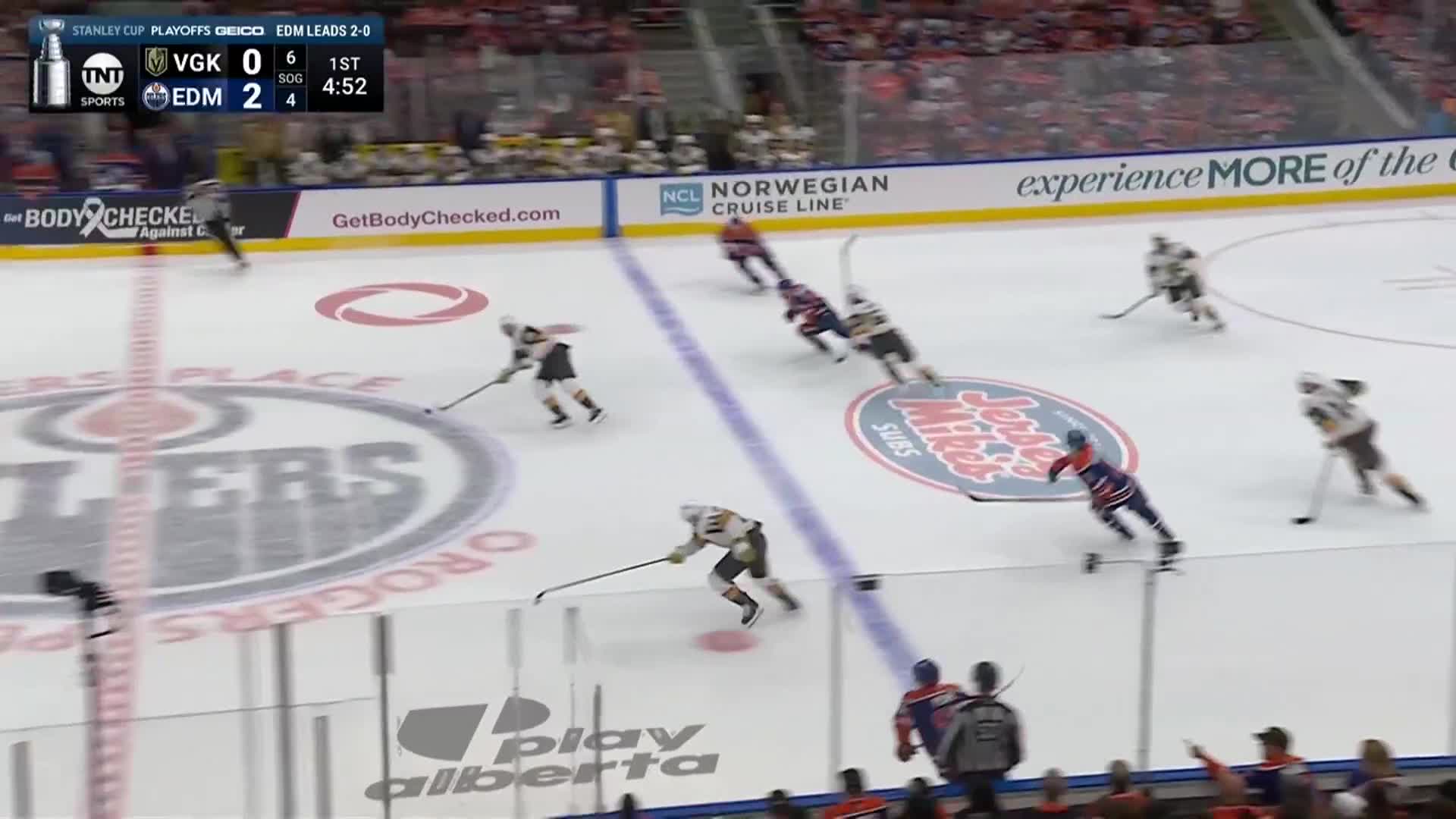 The Edmonton Oilers, in blue and orange, are pushing the puck up the ice. Vegas Golden Knights players, wearing black and gold, are trying to intercept.

