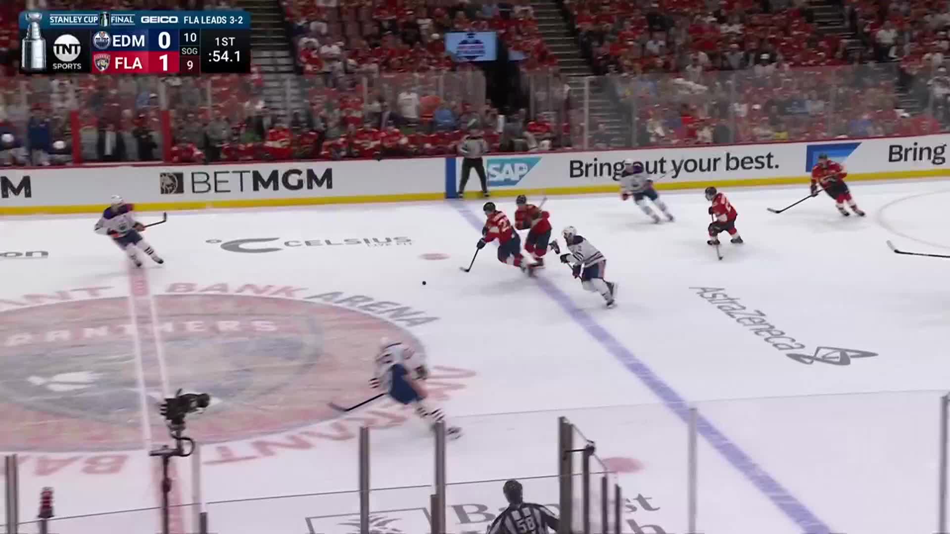 The puck sits loose as a player in red skates toward it, pursued by two in white. A player in white is skating hard down the ice on the left side.
