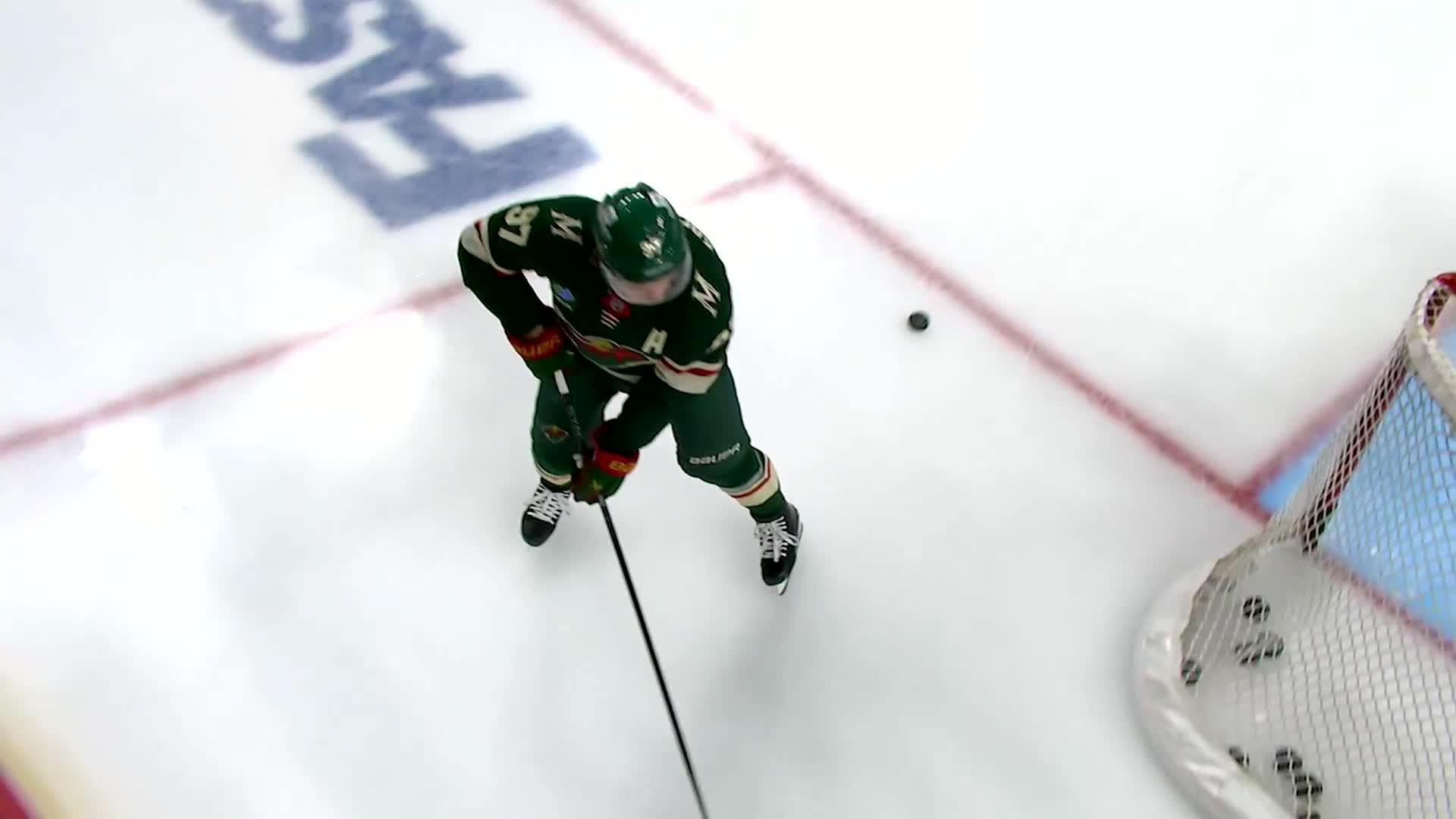 A Minnesota Wild player, stick low, eyes the puck just ahead of him. The black disc is headed for the net, and the goalie is ready.
