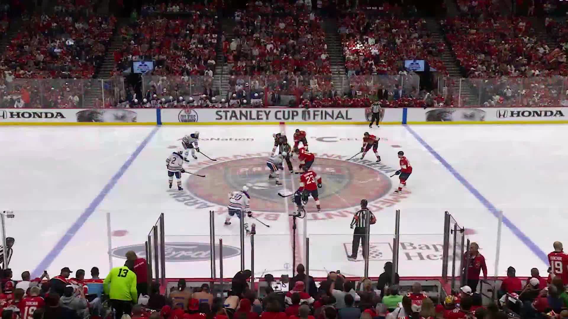 The puck is about to be dropped for a face-off in the center circle, with players from both teams lined up. The crowd in the stands is a sea of red, ready for the Stanley Cup Final.
