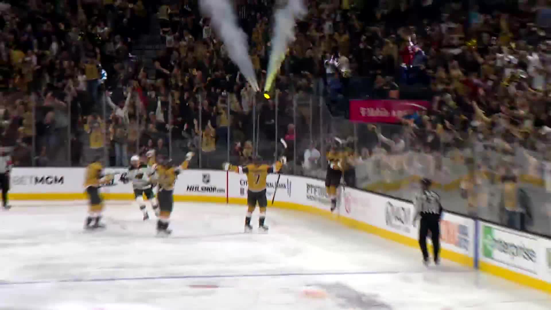Players in black and gold jerseys celebrate on the ice, arms raised in triumph. Above them, the crowd roars, and plumes of smoke rise into the air.
